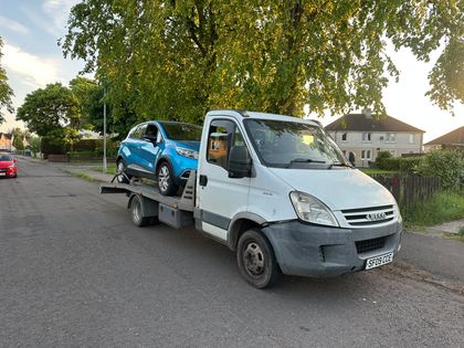 A Roadsist Auto recovery truck with a car loaded on a residential street in North Lanarkshire at dusk